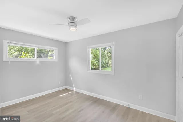 an empty room with wooden floor ceiling fan and windows