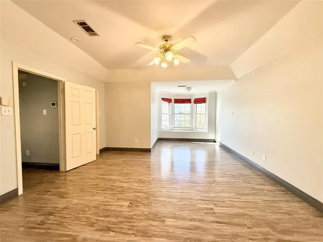 an empty room with wooden floor chandelier fan and windows