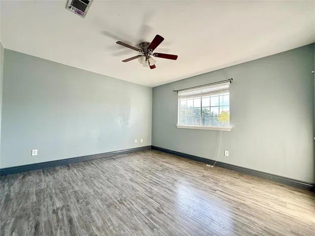 an empty room with wooden floor fan and windows