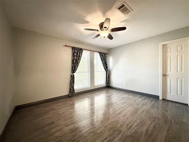an empty room with wooden floor chandelier fan and windows