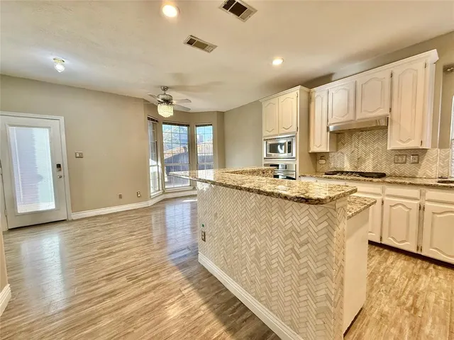 a kitchen with granite countertop a stove a sink and white cabinets with wooden floor