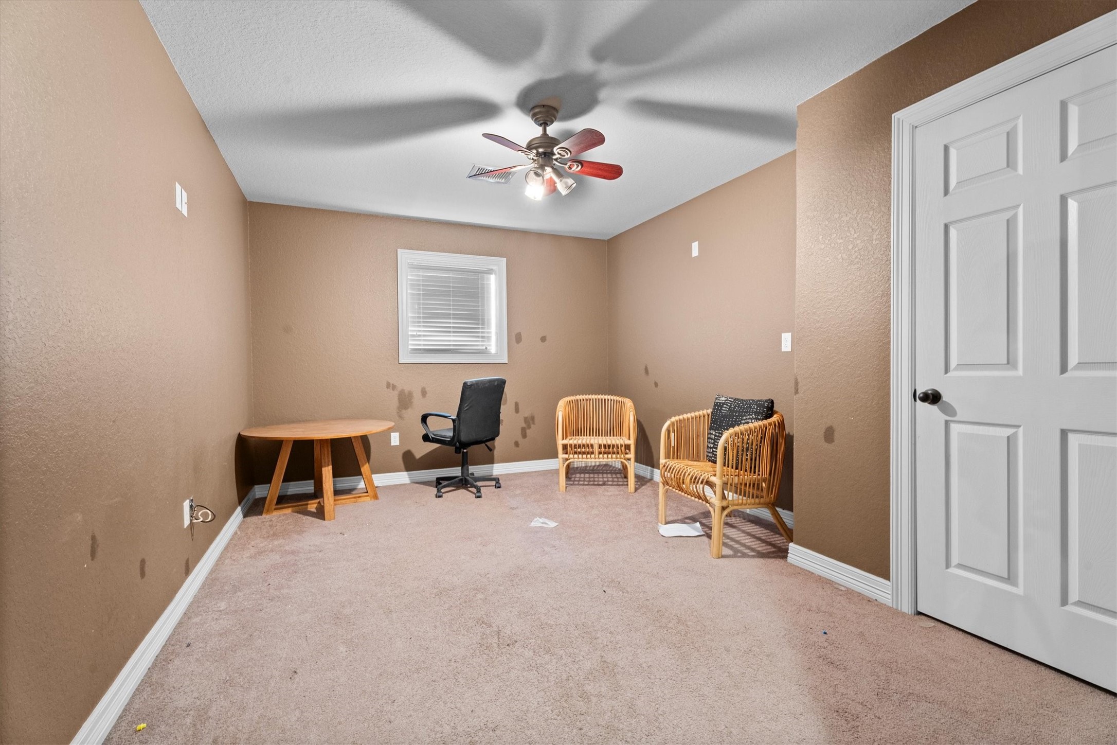 11066 Sh 242 Conroe, TX 77385 - Photo 18 of 21 This room features neutral-toned walls and carpet, with a ceiling fan for comfort. It includes a window for natural light and is furnished with a small round table, office chair, and two wicker chairs, offering a versatile space for various uses.