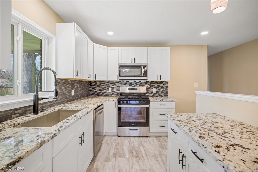 154 Winchester Road Akron, OH 44333 - Photo 12 of 26 Kitchen featuring stainless steel appliances, backsplash, sink, light stone countertops, and white cabinets