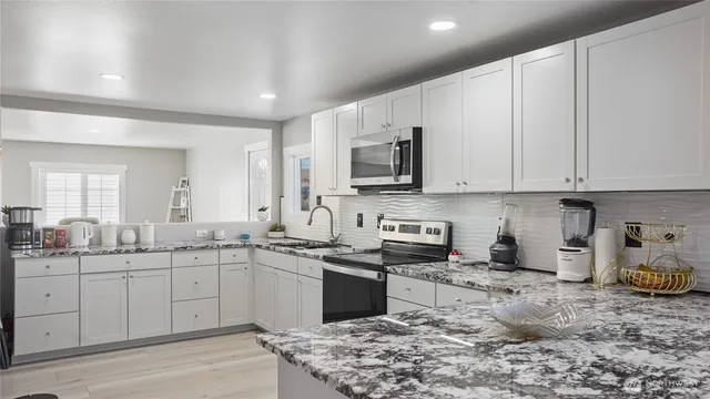 a kitchen with stainless steel appliances granite countertop a sink a stove top oven and white cabinets