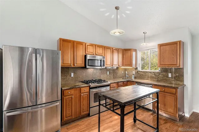 a kitchen with stainless steel appliances granite countertop a refrigerator a sink dishwasher a stove and a refrigerator with wooden floor