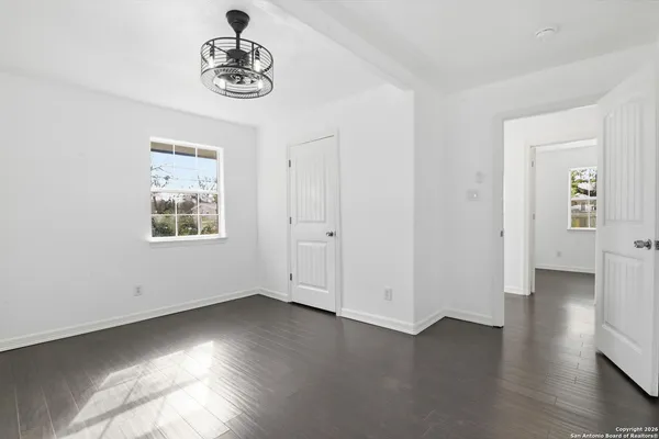 an empty room with wooden floor chandelier fan and windows