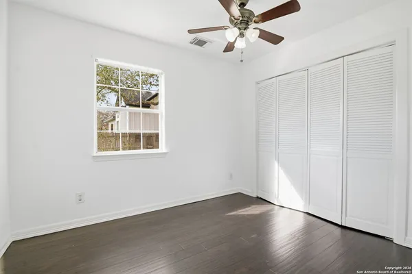 an empty room with wooden floor chandelier fan and windows