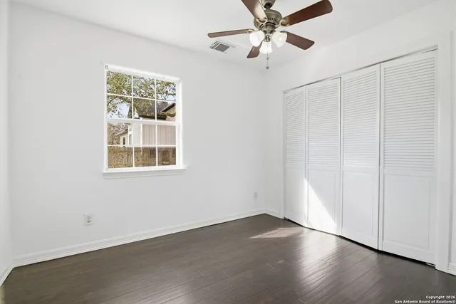 an empty room with wooden floor chandelier fan and windows