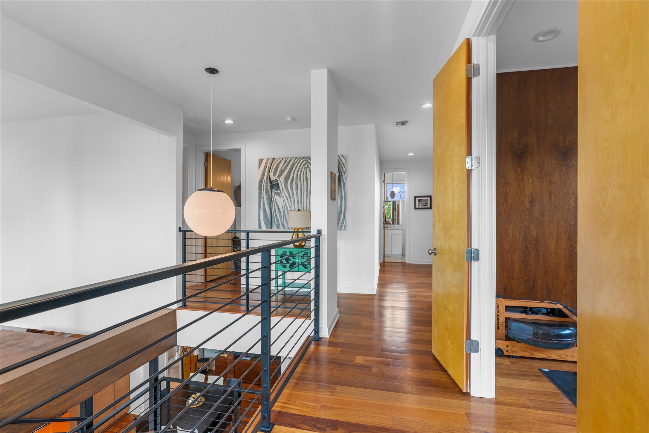 408 Starlight Village Loop Leander, TX 78641 - Photo 29 of 40 Rich hardwood floors lead to a sun-drenched hallway, featuring a stylish staircase with a sleek black railing and an inviting modern light fixture.
