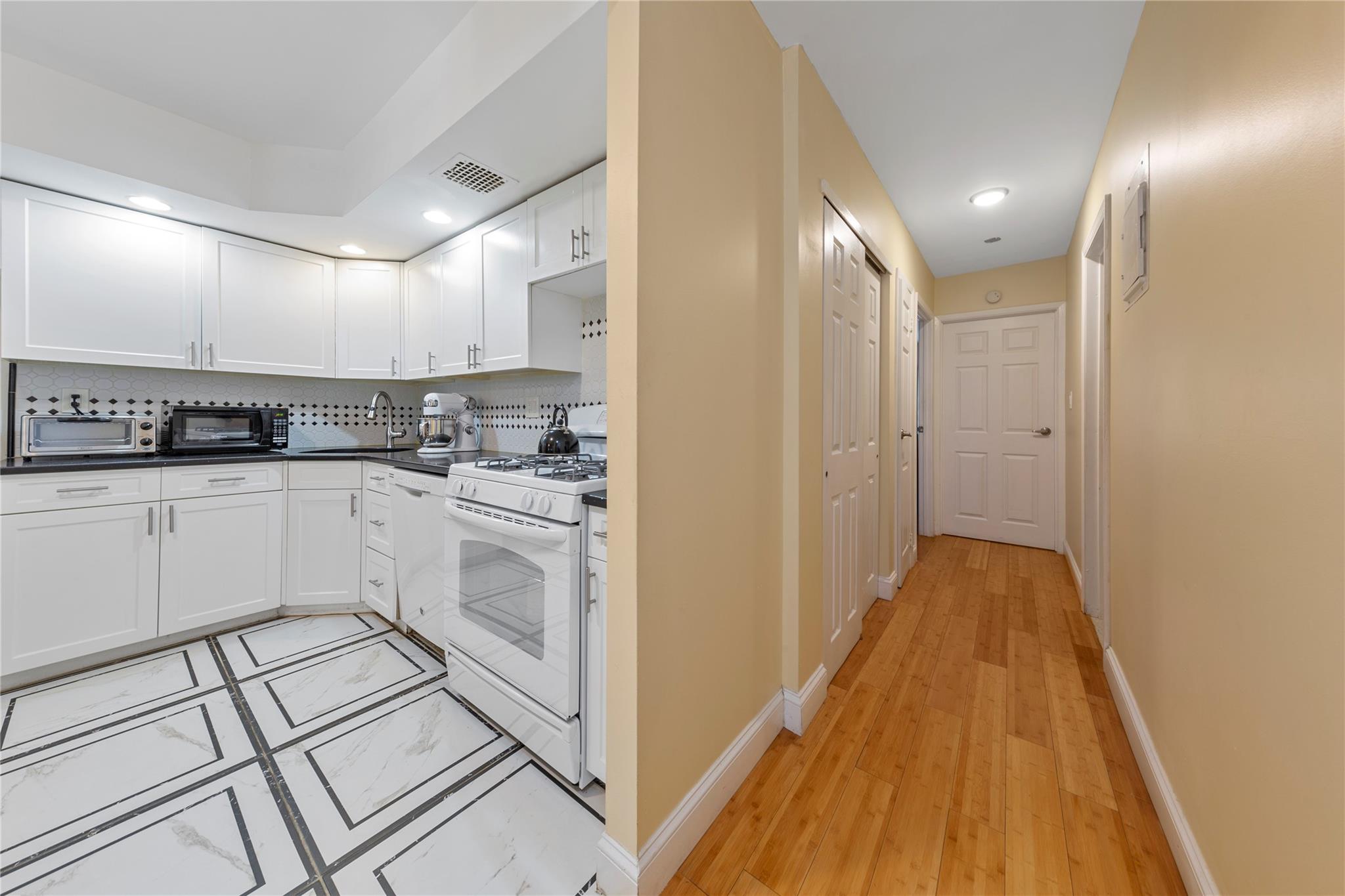 71-09 Sutton Place, Unit 2 Queens, NY 11365 - Photo 15 of 20 Kitchen featuring visible vents, dark countertops, baseboards, white appliances, and white cabinetry