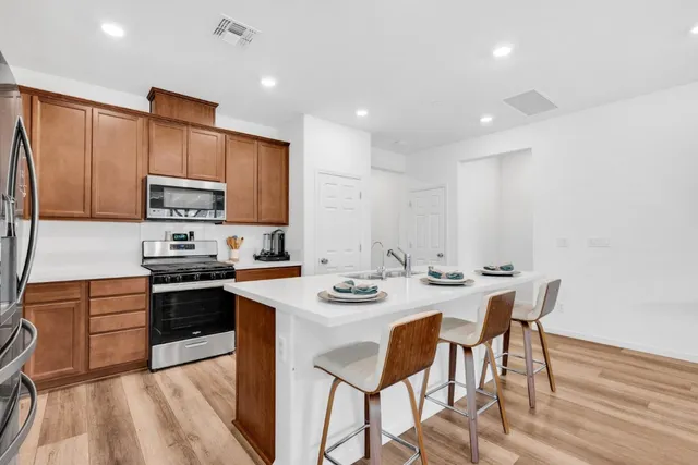 a kitchen with stainless steel appliances granite countertop a stove top oven a sink dishwasher a dining table and chairs with wooden floor