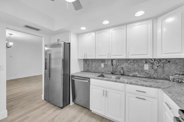 a kitchen with stainless steel appliances granite countertop white cabinets a refrigerator and a sink