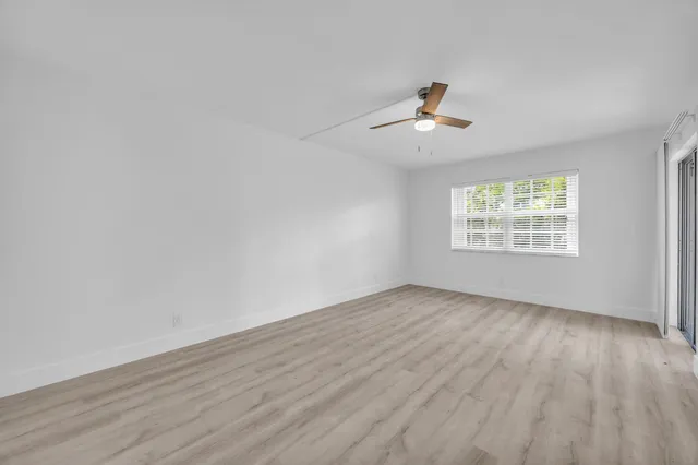 an empty room with wooden floor ceiling fan and windows