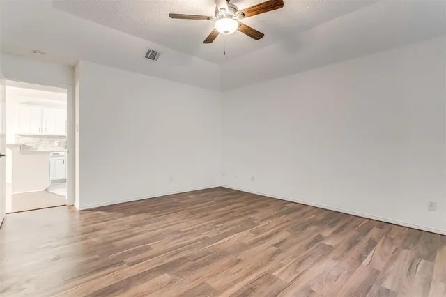 an empty room with wooden floor chandelier fan and windows