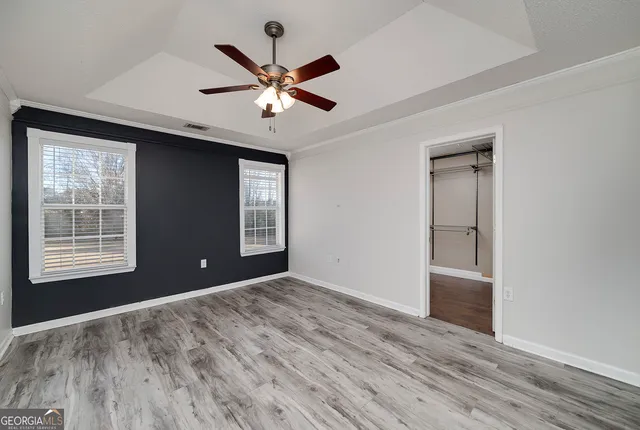a view of an empty room with wooden floor and a ceiling fan