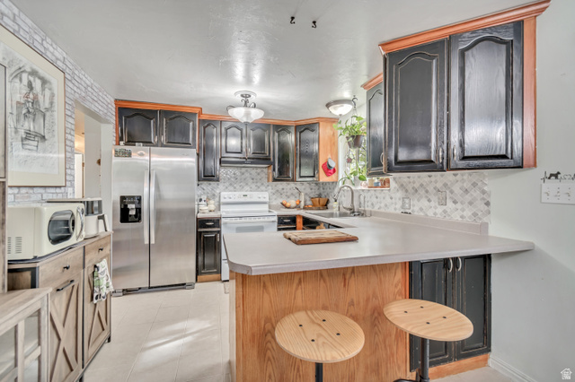 7470 Ramanee Drive Midvale, UT 84047 - Photo 8 of 29 Kitchen featuring light countertops, a peninsula, white appliances, a kitchen bar, and light tile patterned floors