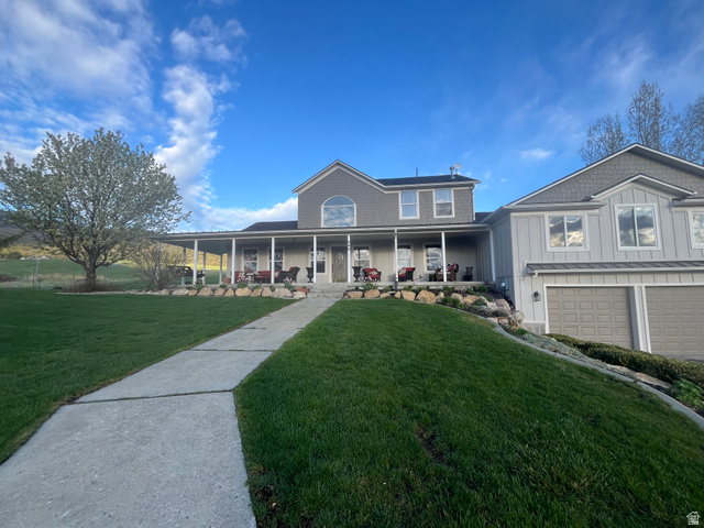 444 North 7200th Street West Mendon, UT 84325 - Photo 1 of 10 Expansive front yard with a concrete pathway leading to a multi-level home featuring a covered front porch, an upper-level arched window, and an attached two-car garage with overhead doors