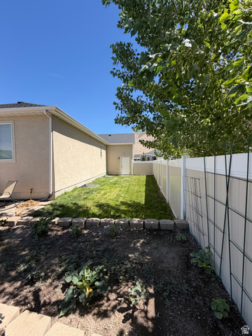 118 Tram Rock Rd. Lake Point, UT 84074 - Photo 33 of 34 Expansive backyard space featuring a manicured lawn, established garden bed with concrete block edging, and a vinyl privacy fence
