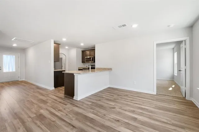 a view of kitchen and empty room with wooden floor