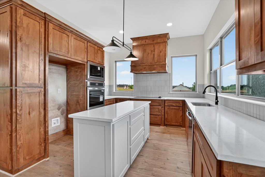 225 Kilkenny Road Poolville, TX 76487 - Photo 12 of 36 Gourmet kitchen featuring a central island with a white countertop, extensive wood cabinetry, built-in stainless steel appliances, a tile backsplash, and wood-finish flooring