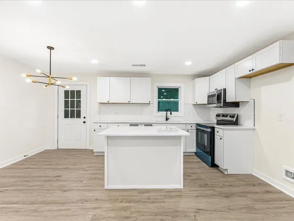 a kitchen with stainless steel appliances granite countertop a stove a sink dishwasher a refrigerator and white cabinets with wooden floor