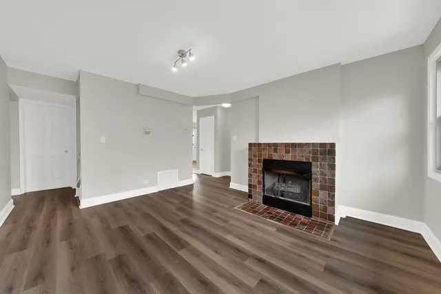 a view of an empty room with wooden floor fireplace and a window