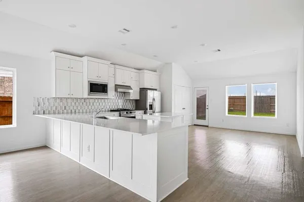 a kitchen with stainless steel appliances a stove top oven a sink a refrigerator with white cabinets and wooden floor