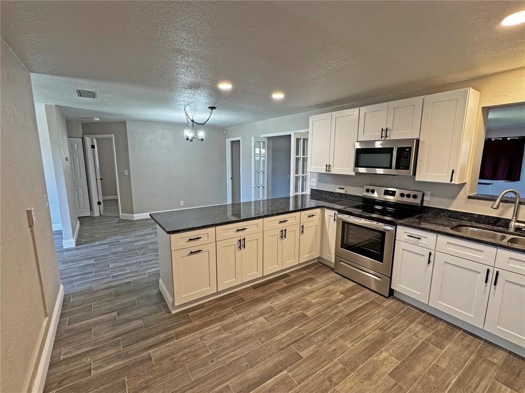 1421 Suwanee Road Daytona Beach, FL 32114 - Photo 7 of 21 a large white kitchen with granite countertop a stove top oven a sink and dishwasher with wooden floor