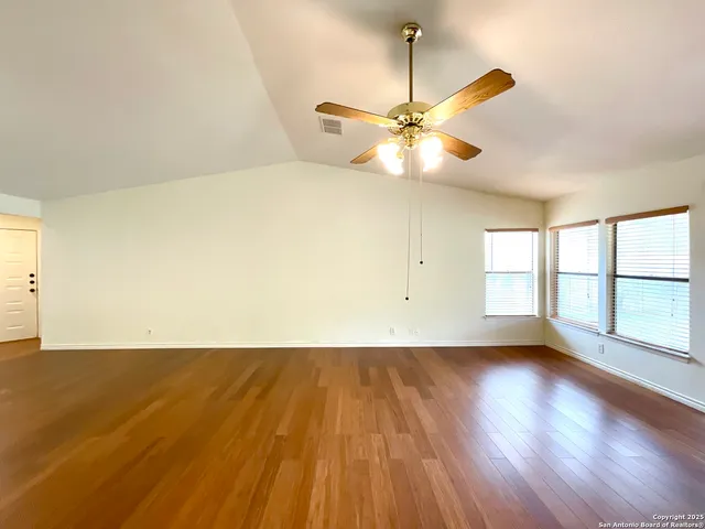 an empty room with wooden floor fan and windows