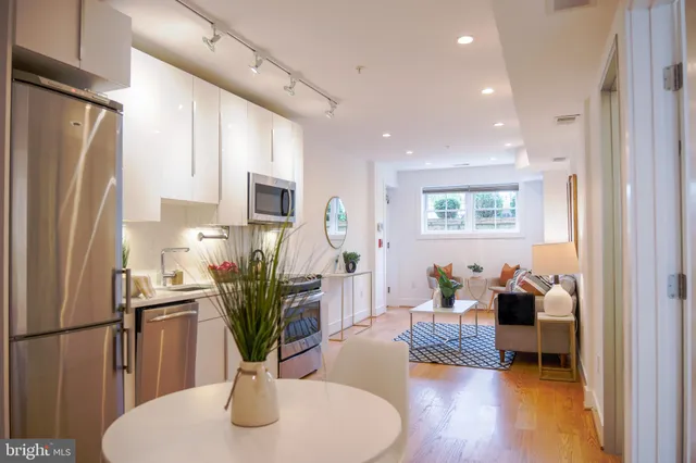 a living room with stainless steel appliances furniture wooden floor and a view of kitchen