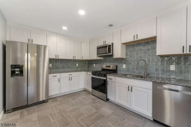 a kitchen with stainless steel appliances kitchen island granite countertop a stove a sink and a white cabinets