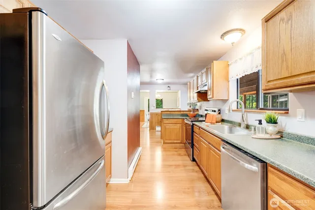 a kitchen with stainless steel appliances a refrigerator a sink dishwasher a stove with wooden cabinets and floor