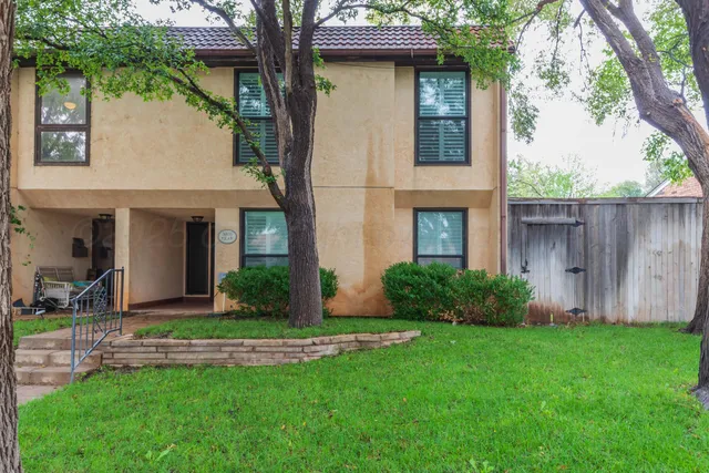 a view of a house with brick walls and a yard with plants and a large tree