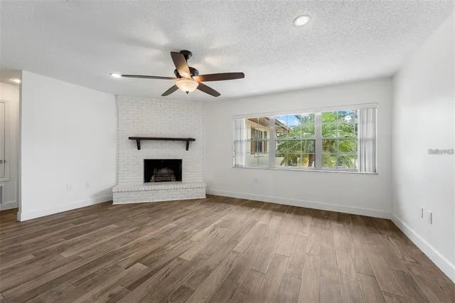 an empty room with wooden floor chandelier fan and windows