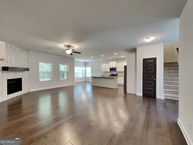 a view of an empty room with wooden floor and a kitchen