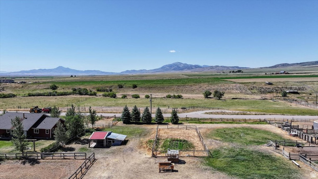 1634 West Arimo Road Arimo, ID 83214 - Photo 83 of 89 Expansive rural property featuring a red-sided residence with a dark roof, multiple fenced enclosures, mature trees, and outbuildings, all set against a backdrop of distant mountains