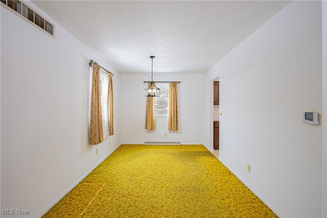 5905 Renninger Road New Franklin, OH 44319 - Photo 7 of 31 Unfurnished dining area with carpet floors, a baseboard radiator, a textured ceiling, and a notable chandelier