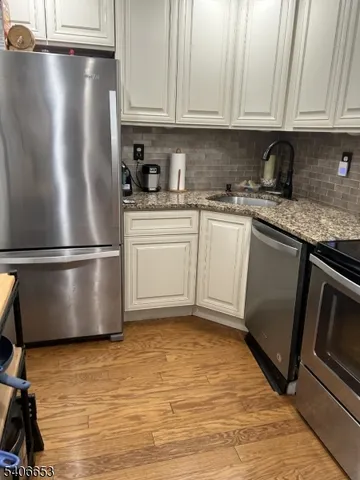 a kitchen with stainless steel appliances granite countertop a refrigerator a sink a stove and white cabinets