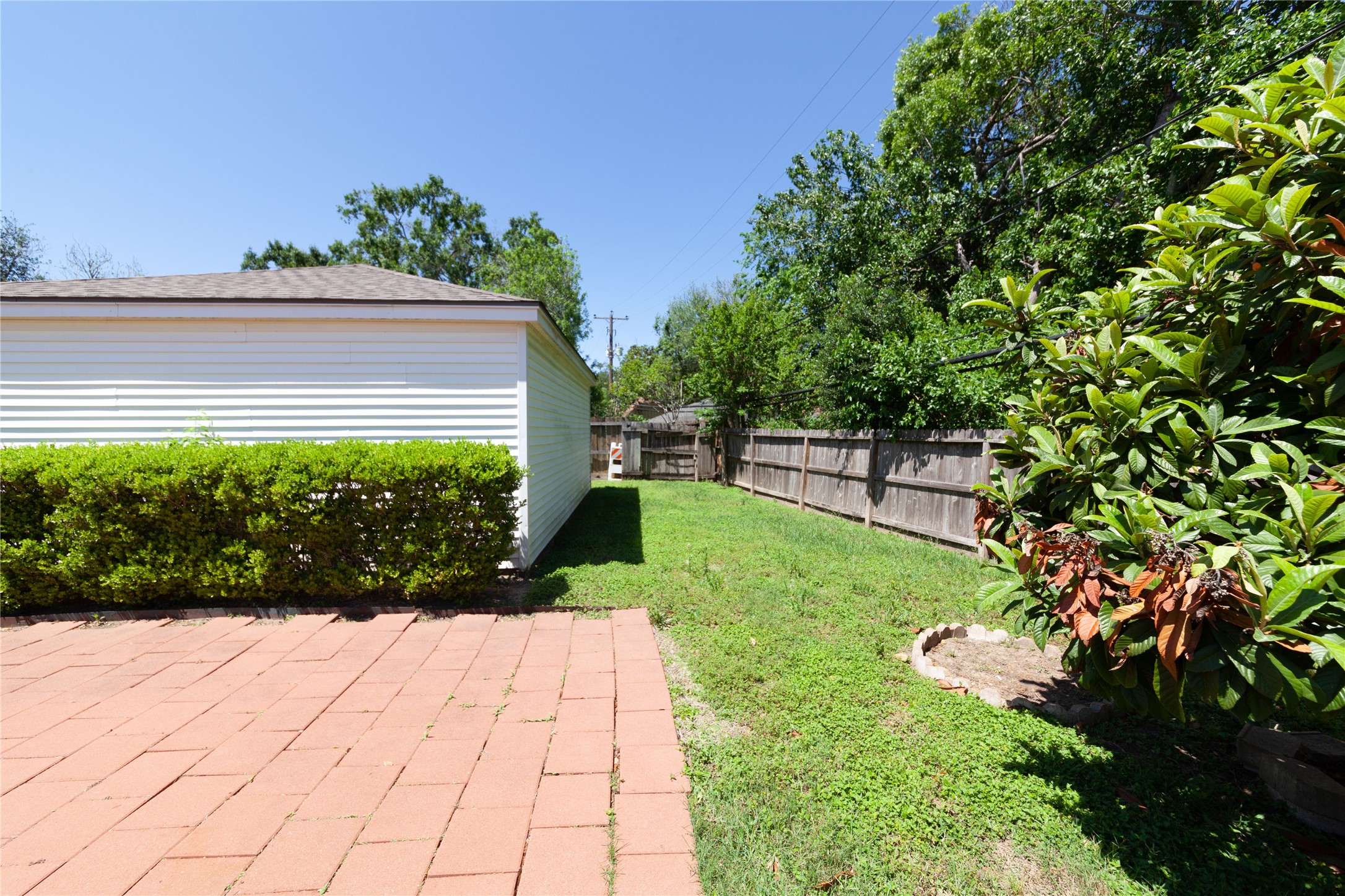 8826 Roos Road Houston, TX 77036 - Photo 41 of 42 A backyard with a paved patio area, a small lawn, and a wooden fence. There's also a white-sided building, possibly a garage or shed, and some greenery including bushes and trees, providing a private and tranquil outdoor space.
