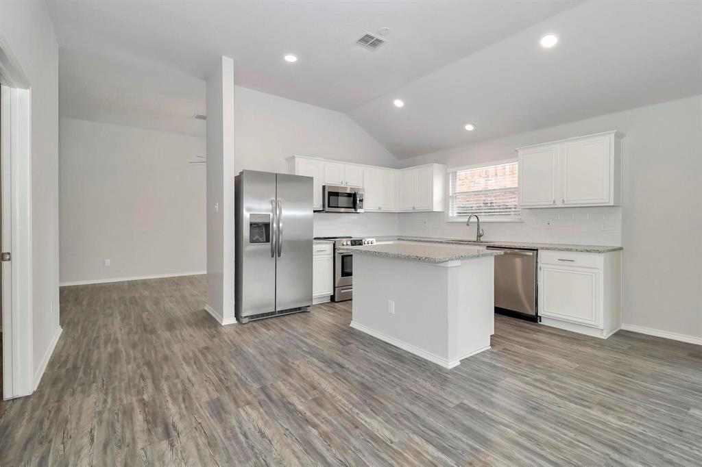 5528 Ridge View Drive Watauga, TX 76137 - Photo 8 of 16 Kitchen featuring stainless steel appliances, white cabinets, backsplash, light wood-style flooring, and vaulted ceiling
