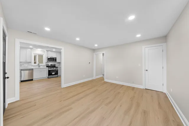 a view of an empty room and kitchen with wooden floor