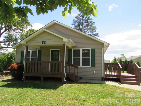 a view of a house with a yard plants and large tree
