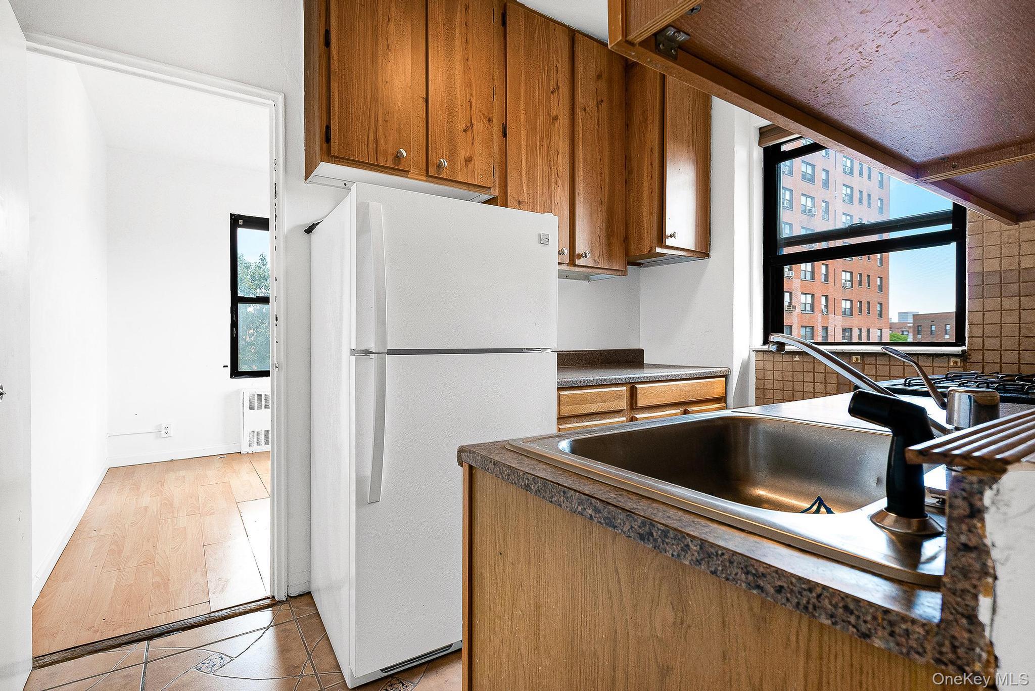 99-32 66th Road, Unit 5B Queens, NY 11374 - Photo 9 of 27 Kitchen with brown cabinetry, freestanding refrigerator, dark countertops, and plenty of natural light