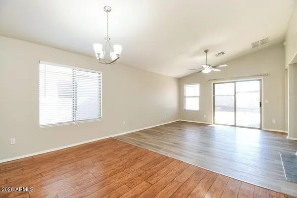 an empty room with wooden floor chandelier fan and windows