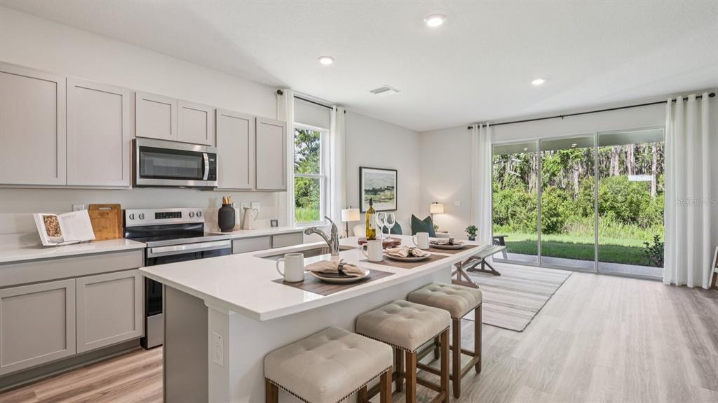 32516 Welling Blade Loop Wesley Chapel, FL 33545 - Photo 11 of 39 a kitchen with a stove a sink a microwave a dining table and chairs