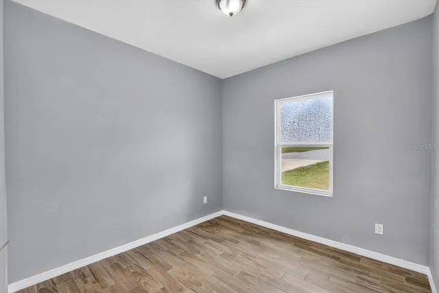 a view of an empty room with wooden floor and a bathroom