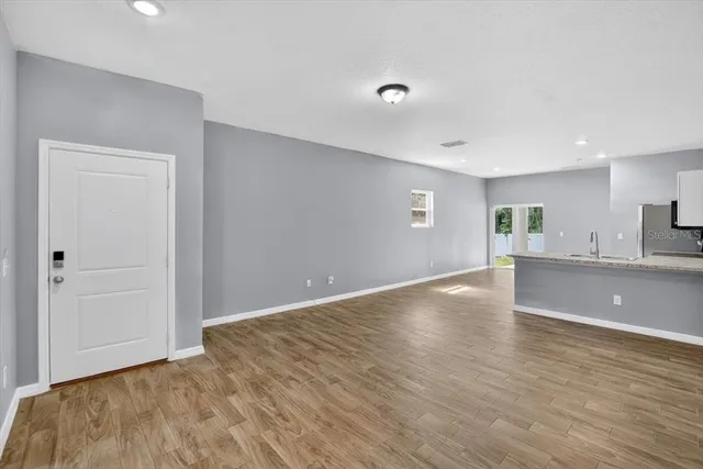 a view of an empty room with wooden floor and kitchen