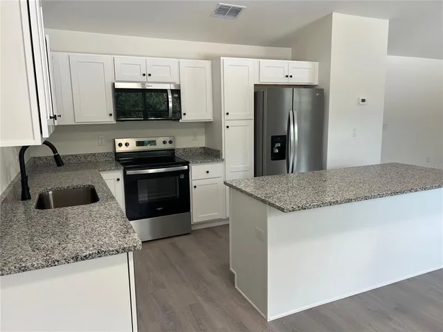 a kitchen with granite countertop a sink a microwave a refrigerator and cabinetry