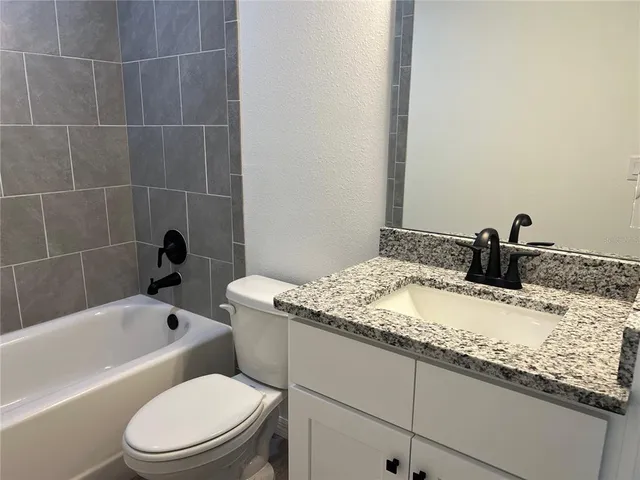 a bathroom with a granite countertop bathtub sink vanity mirror and toilet