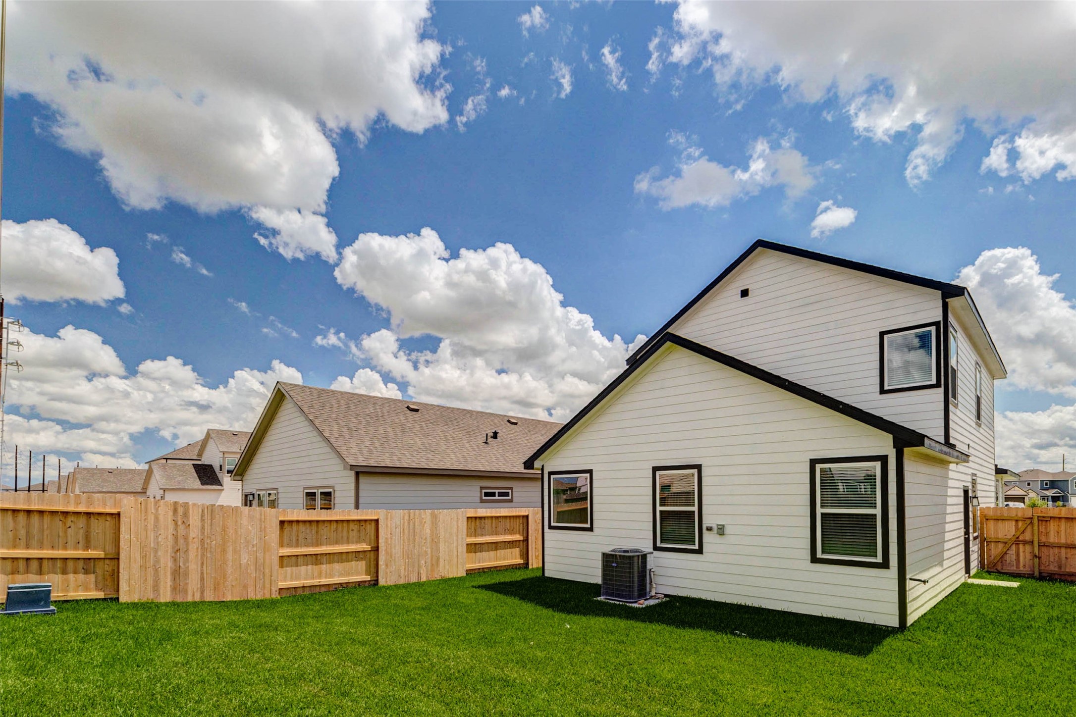 6471 Escondido Drive Rosharon, TX 77583 - Photo 30 of 33 Rear exterior view showcasing the home’s crisp white siding, black trim, fenced backyard, green lawn, and bright sky backdrop. The yard offers usable outdoor space for pets, play, grilling, or relaxing, with side access and a clean new construction exterior.